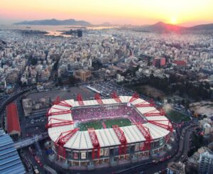 Aerial view of Georgios Karaiskakis Stadium in Piraeus at sunset, full crowd before Olympiacos vs Real Madrid.