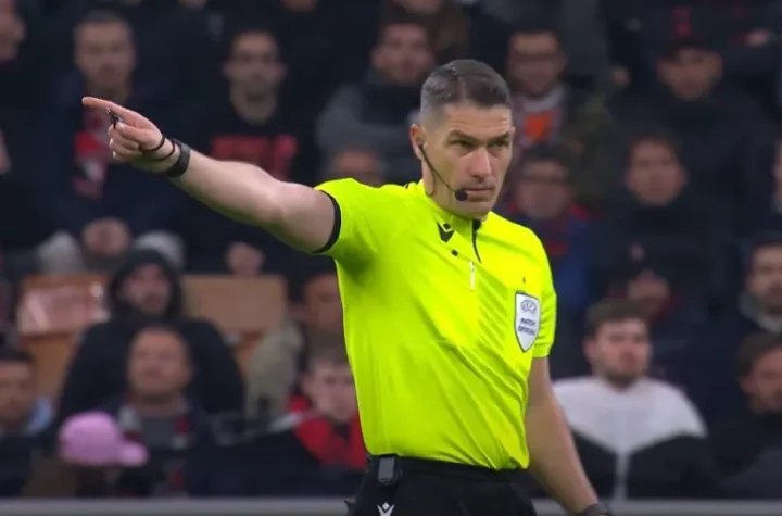 Referee in neon kit points to indicate a restart amid a packed crowd.