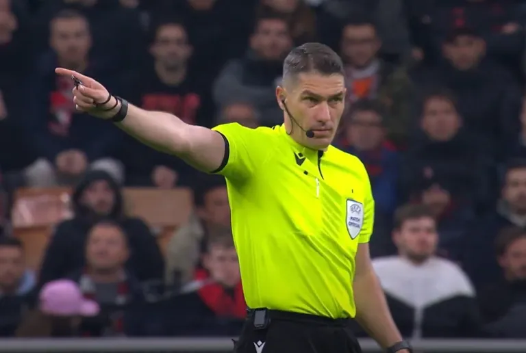 Referee in neon kit points to indicate a restart amid a packed crowd.