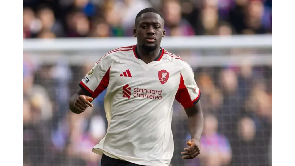 Ibrahima Konate Real Madrid- Liverpool defender in a white and red away kit running during a match, with the crowd blurred in the background.