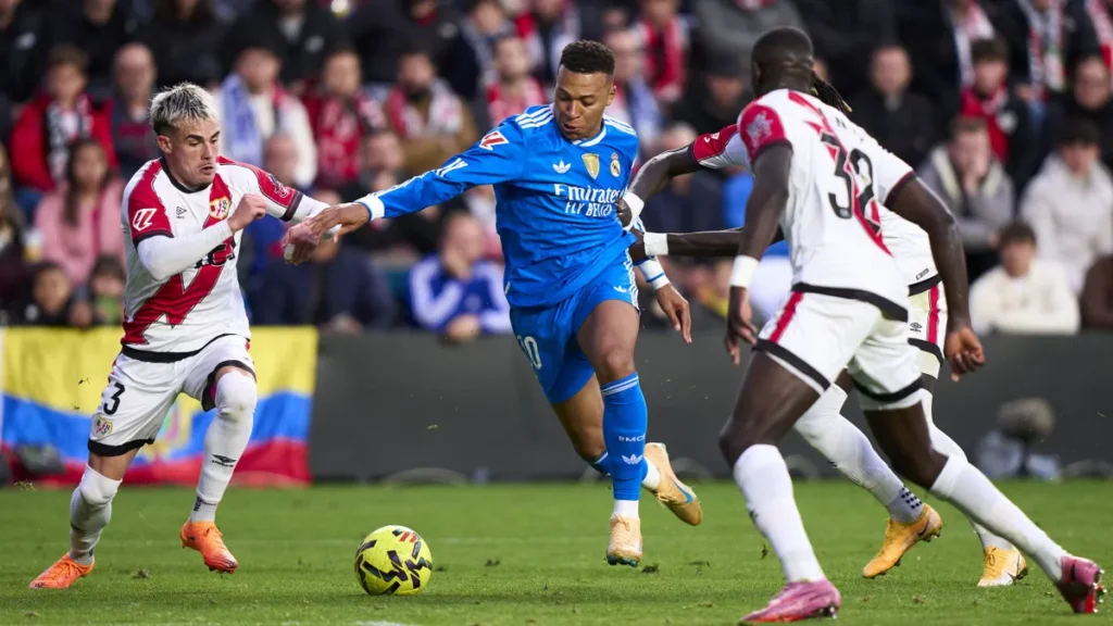 Kylian Mbappé dribbles between Rayo Vallecano defenders at Vallecas.