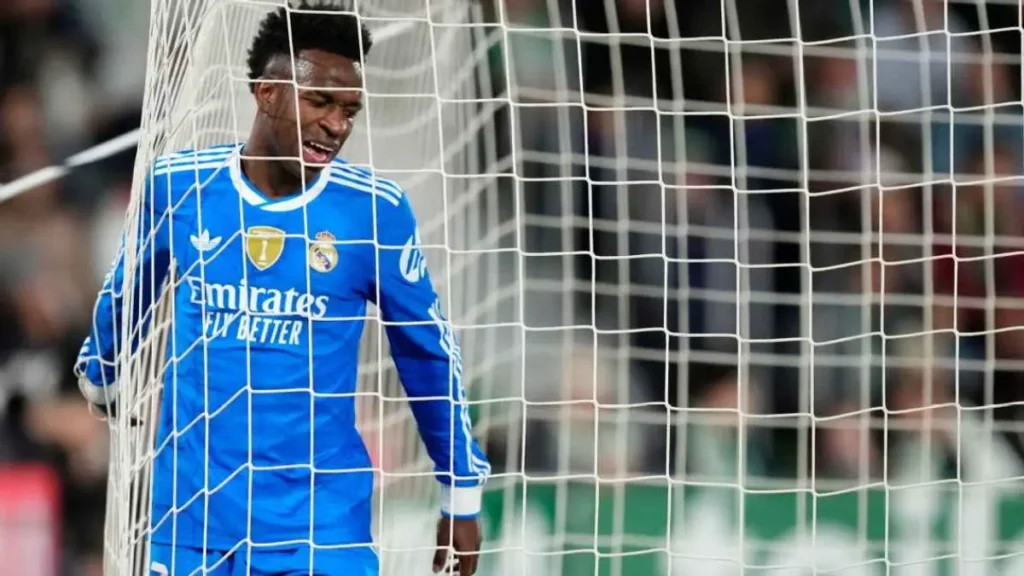 Real Madrid forward in a blue away kit standing pressed against the goal net with eyes closed in frustration during a match. Vinicius contract renewal with Real Madrid