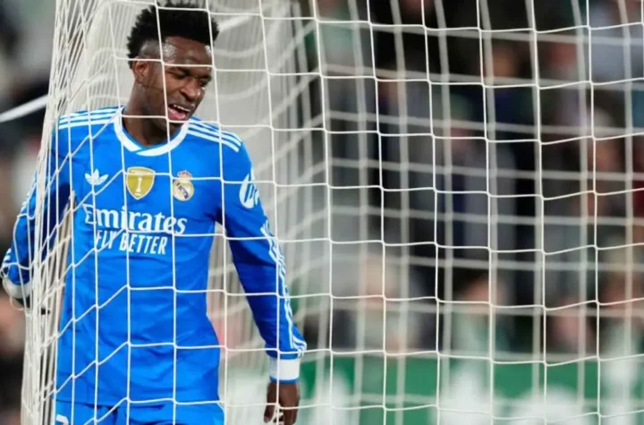 Real Madrid forward in a blue away kit standing pressed against the goal net with eyes closed in frustration during a match. Vinicius contract renewal with Real Madrid