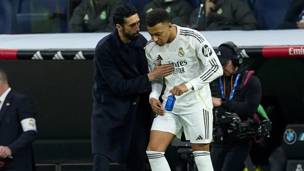 A Real Madrid coach talks to a player in white near the bench during a La Liga match after the player leaves the field.