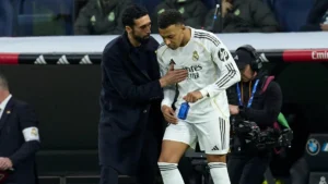 A Real Madrid coach talks to a player in white near the bench during a La Liga match after the player leaves the field.