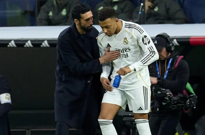 A Real Madrid coach talks to a player in white near the bench during a La Liga match after the player leaves the field.