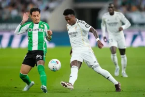 Real Madrid player in white controls the ball under pressure from a Real Betis defender during the Real Madrid vs Real Betis match, with another Madrid player in the background.