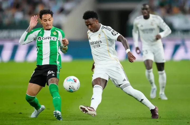 Real Madrid player in white controls the ball under pressure from a Real Betis defender during the Real Madrid vs Real Betis match, with another Madrid player in the background.