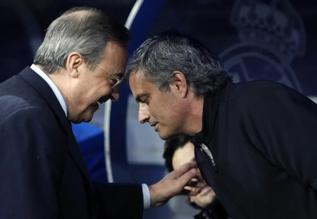 Two senior football figures greet at a Real Madrid event as coaching speculation around the club intensifies.