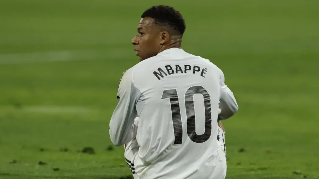 A Real Madrid player in a white No. 10 shirt sits on the field and looks over his shoulder during a match.