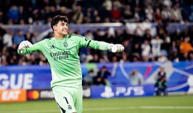 Real Madrid goalkeeper celebrates during the UEFA Youth League final in a green kit with fans in the background.