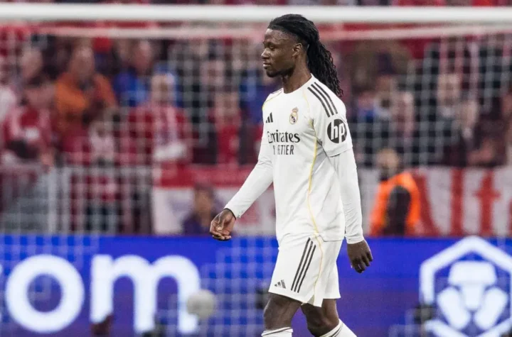 Real Madrid player walking on the pitch during a match with the goal net in the background.