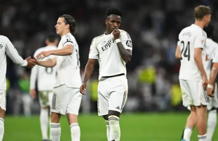 Real Madrid players stand on the pitch during a tense match moment, with one player centered and teammates around him