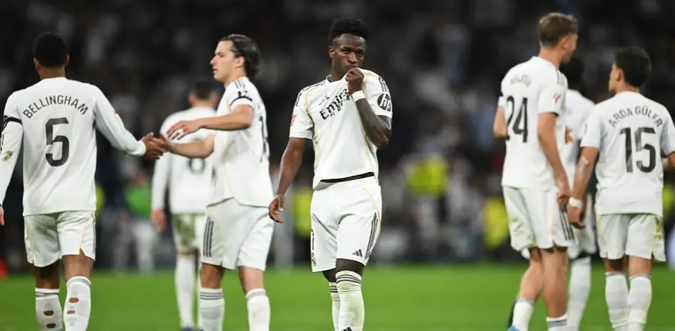 Real Madrid players stand on the pitch during a tense match moment, with one player centered and teammates around him