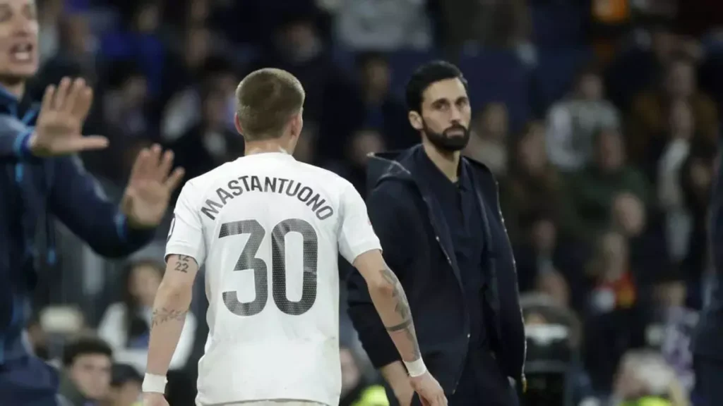 Real Madrid player wearing a shirt with “Mastantuono 30” on the back walks past the coach on the touchline during a match