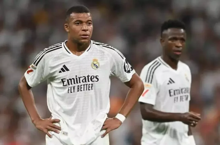 Two Real Madrid players stand on the pitch during a match with serious expressions.