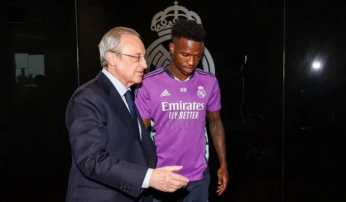 Senior Real Madrid official walking alongside a first-team player in training gear inside a club facility