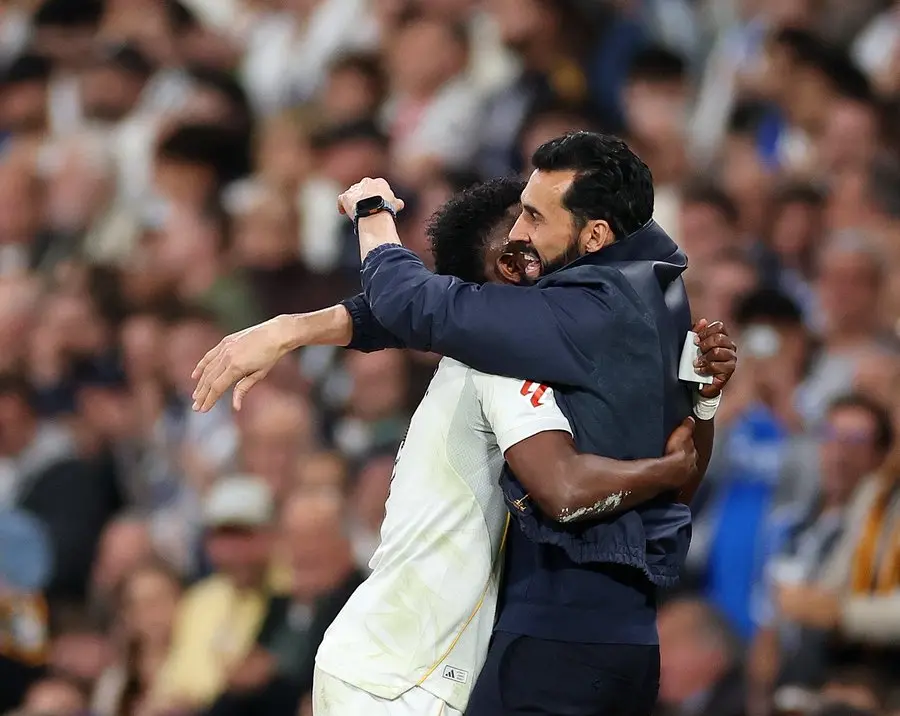 A coach in a dark jacket hugs a Real Madrid player on the pitch after the match