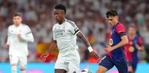 Vinicius El Clasico: Vinicius Jr in a Real Madrid kit runs with the ball as a Barcelona player tracks him during a match