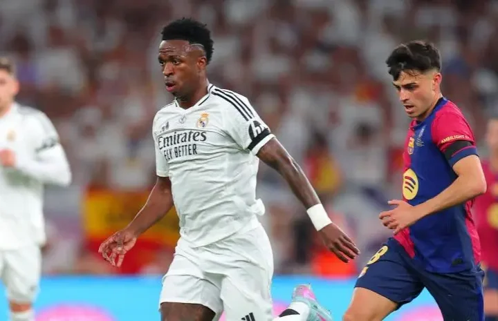 Vinicius El Clasico: Vinicius Jr in a Real Madrid kit runs with the ball as a Barcelona player tracks him during a match