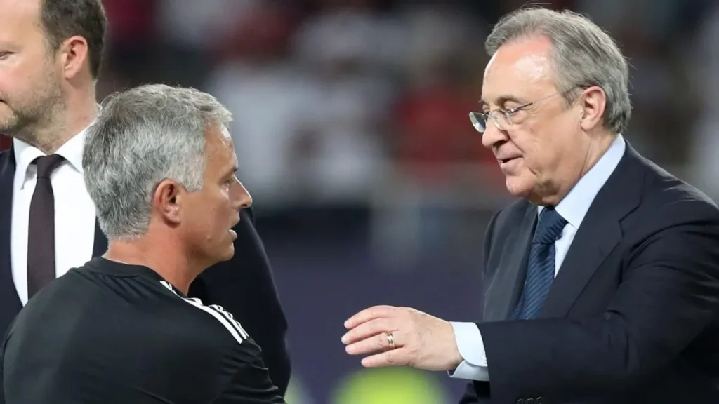 A football coach speaks with a club executive on the touchline during a match.