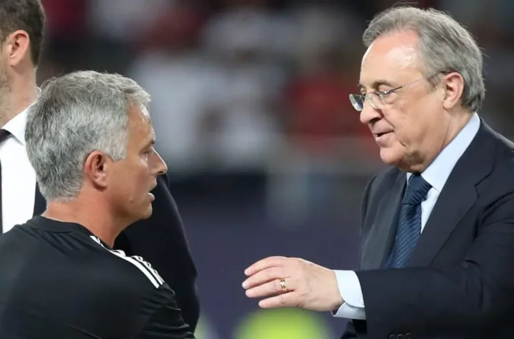 A football coach speaks with a club executive on the touchline during a match.