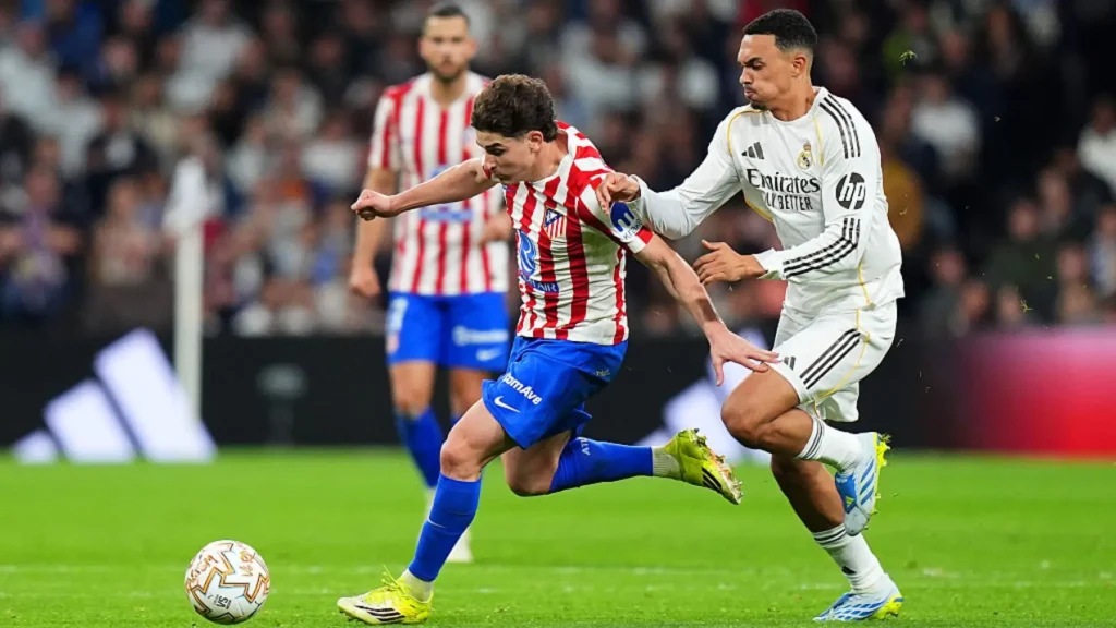 Young player in Atletico Madrid stripes challenged by a Real Madrid player during a match