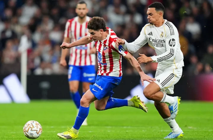 Young player in Atletico Madrid stripes challenged by a Real Madrid player during a match