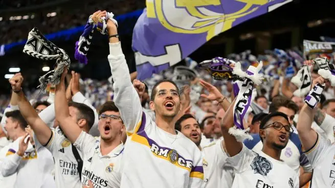 Real Madrid fans cheer in the stands with scarves and flags during a match at the Santiago Bernabéu