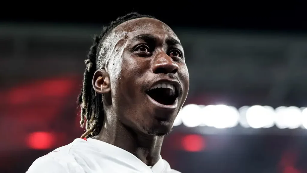 Close-up of a smiling footballer in a white jersey under stadium lights, illustrating the Yan Diomande Real Madrid transfer story.