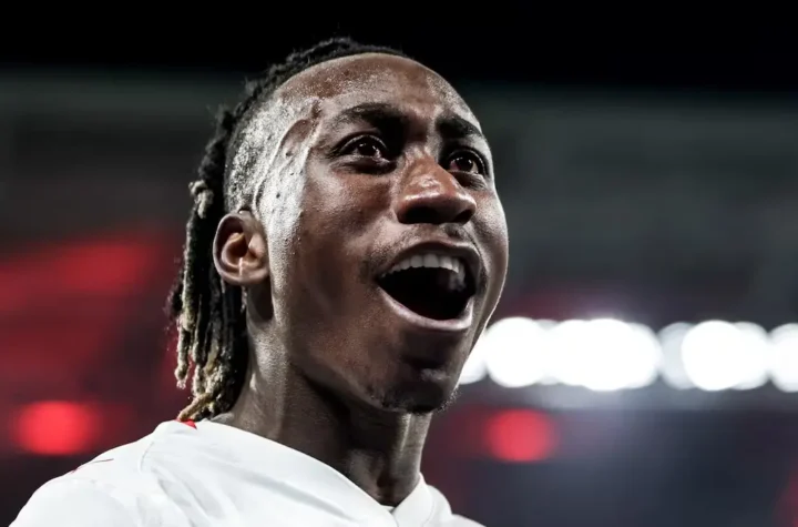Close-up of a smiling footballer in a white jersey under stadium lights, illustrating the Yan Diomande Real Madrid transfer story.